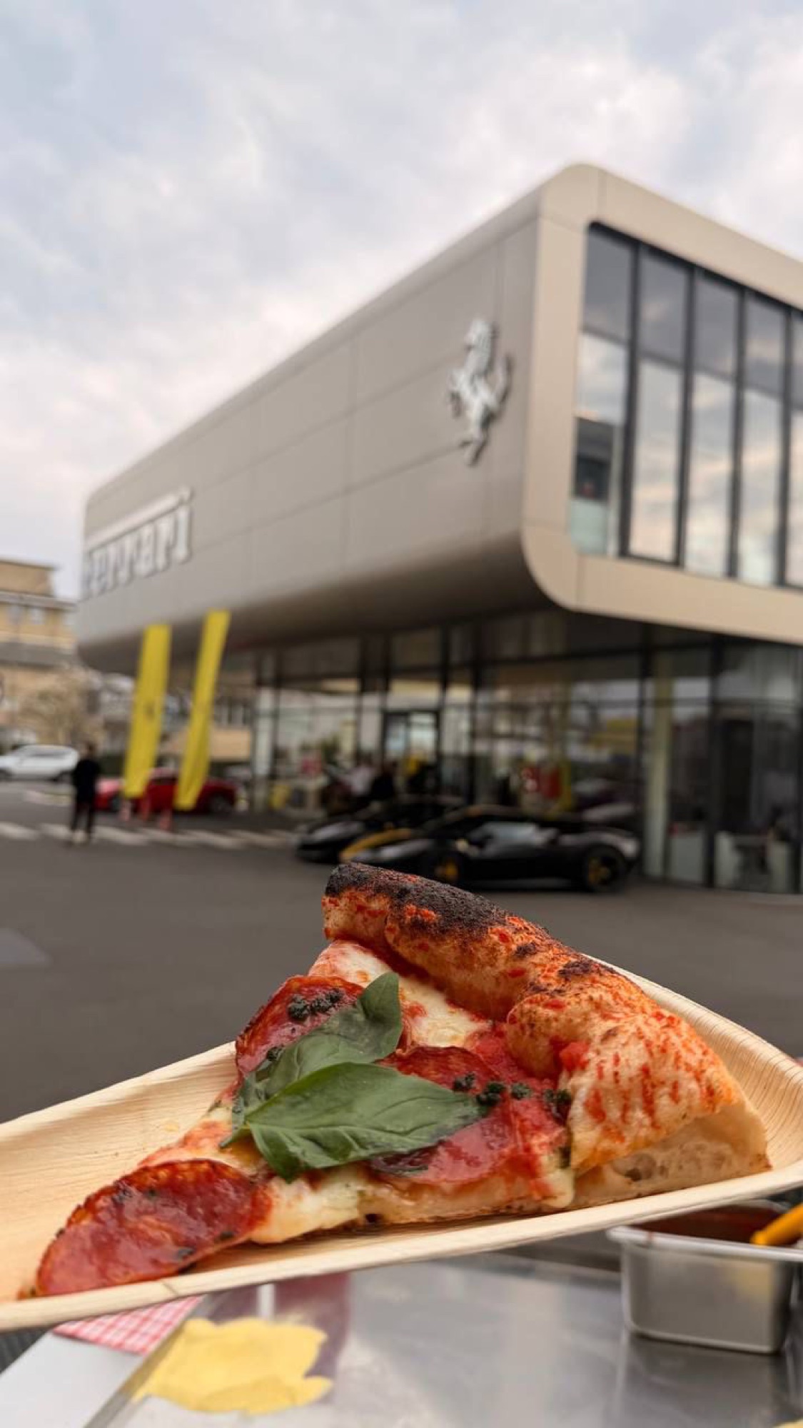 Pizzastück im Vordergrund bei einer Firmenveranstaltung, im Hintergrund ein Autohaus mit Sportwagen