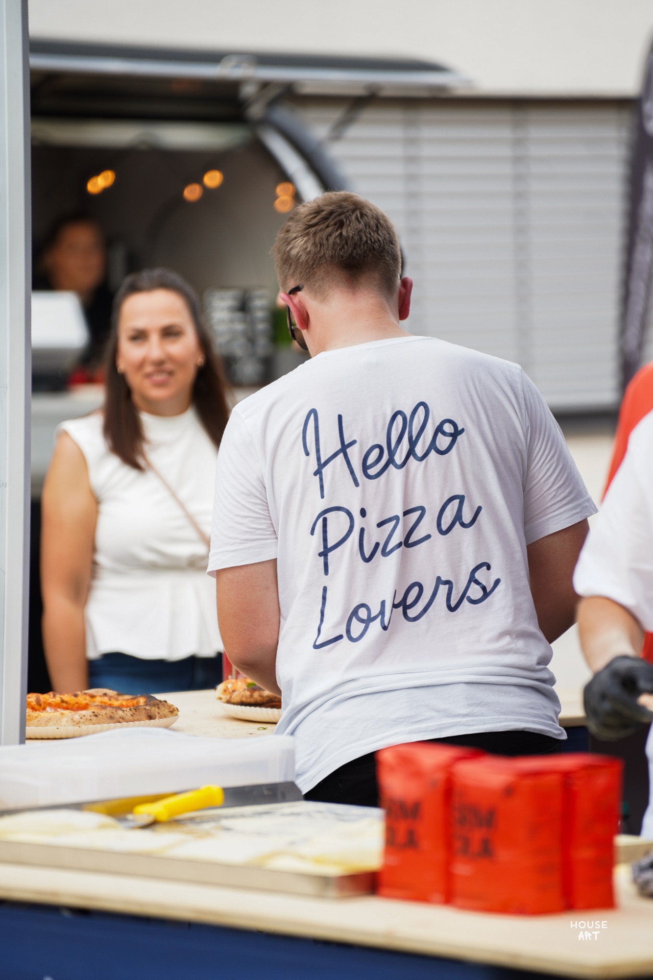Pizza-Ausgabe bei einer Hochzeitsfeier, Gast im „Hello Pizza Lovers“-Shirt am Foodtruck